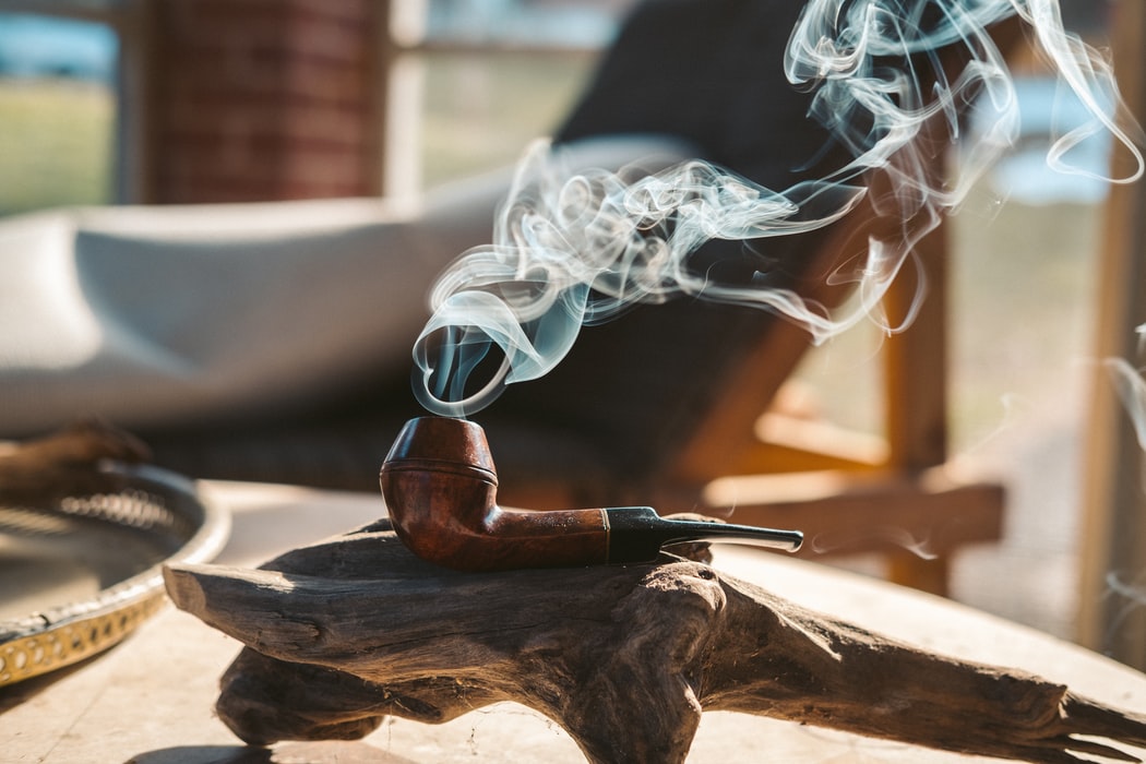 A smoking pipe on a piece of wood with smoke from the bowl